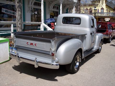1972 Ford Ranchero - A silver GMC pickup truck is parked on a street with other vehicles and buildings in the background.