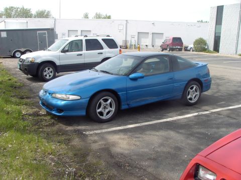 1989 Ford Probe - A blue coupe with a black roof is parked in a lot next to a white SUV and a trailer.