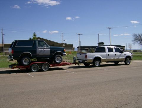 2000 Ford F-250 - A Ford F-250 tows a Ford Bronco on a trailer under a blue sky.