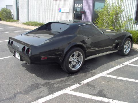 1989 Ford Probe - A black Chevrolet Corvette is parked in a lot outside a building with the number 9849 on the door.
