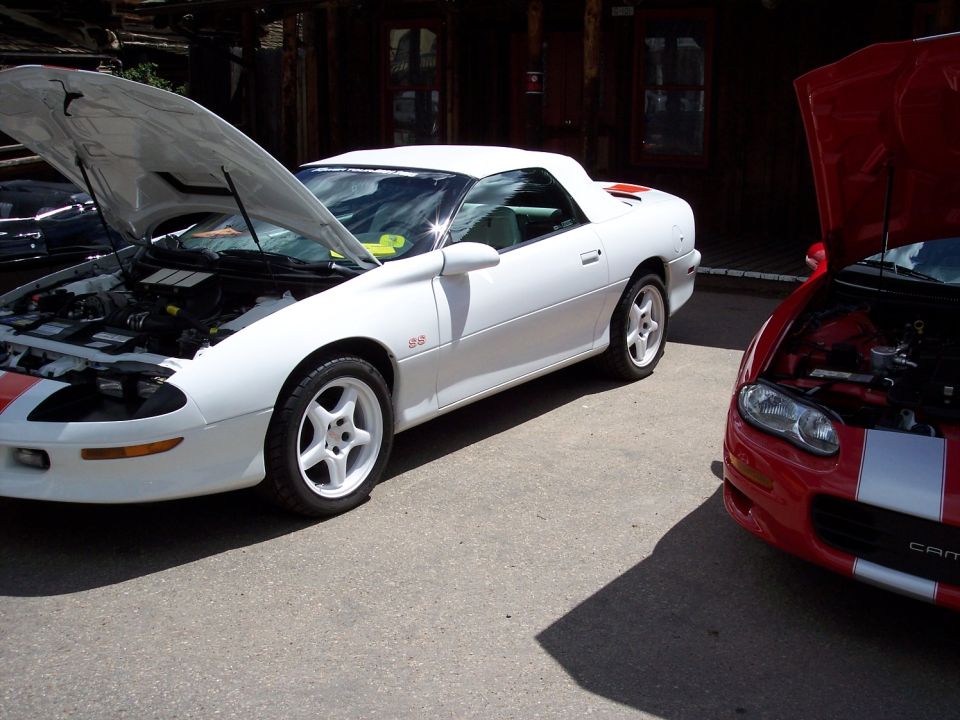 White Camaro with hood open, red Camaro next to it with hood open