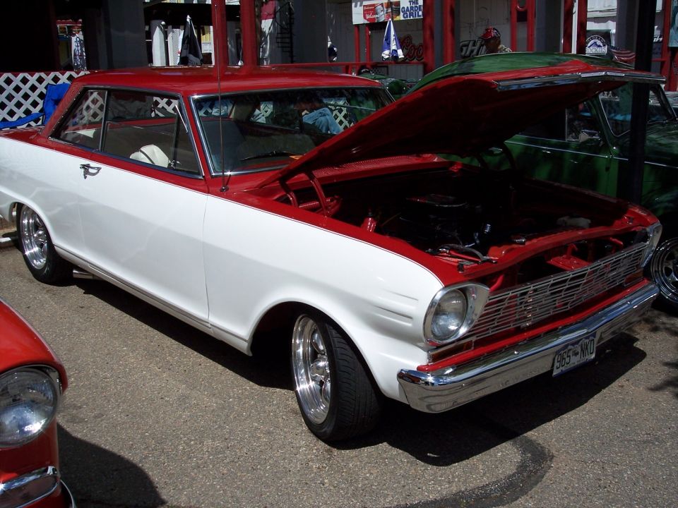 Red and white 1966 Chevrolet Nova coupe with hood open, parked next to a green car