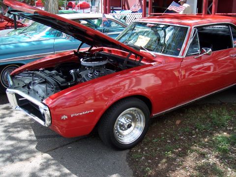1972 Ford Ranchero - A red 1967 Pontiac Firebird is displayed with its hood open, revealing the engine. A second vehicle is parked behind it.