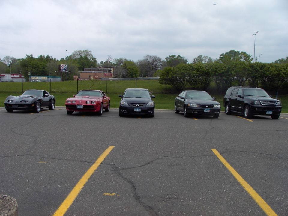 Black Corvette, red Pontiac Firebird, black Mazda, black sedan, and black SUV parked in a lot