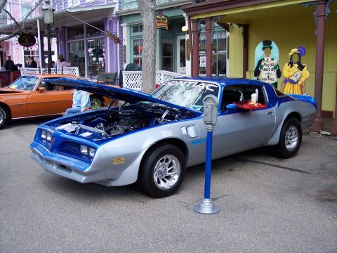 1972 Ford Ranchero - A two-tone silver and blue 1977 Pontiac Firebird Trans Am is parked with its hood up, next to an orange car.