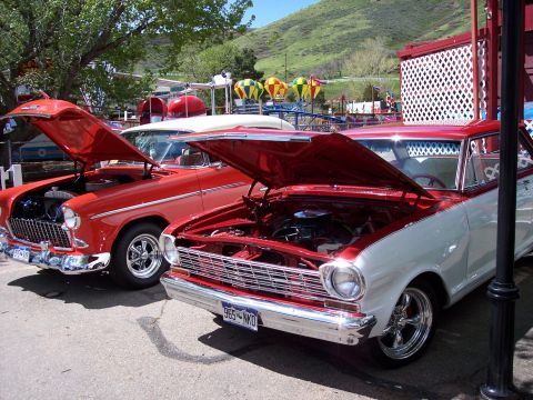 1972 Ford Ranchero - Two classic cars, a red 1955 model and a red and white two-tone model, are parked with their hoods open on a sunny day.