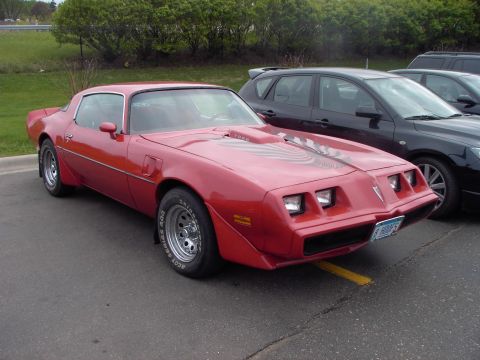 1989 Ford Probe - A red 1977 Pontiac Firebird Trans Am is parked in a lot, with another car visible behind it.