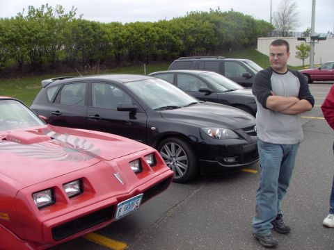 1989 Ford Probe - A red 1977 Pontiac Firebird Trans Am is parked in a lot next to other vehicles and a man.