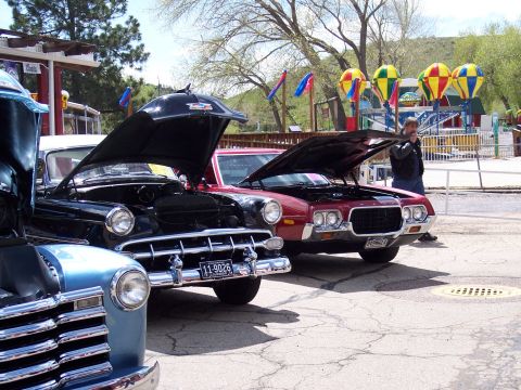 1972 Ford Ranchero - Several classic vehicles are displayed with their hoods up at an outdoor event, with amusement park attractions in the distance.