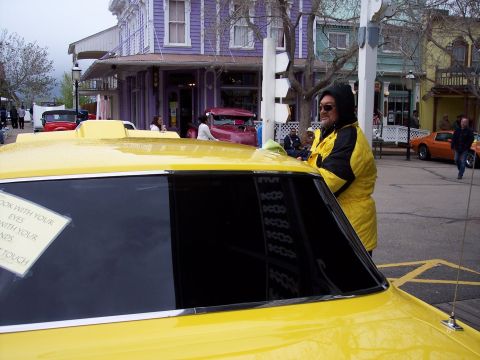 1972 Ford Ranchero - A man cleans a yellow car parked on a street with vintage-style buildings in the background.