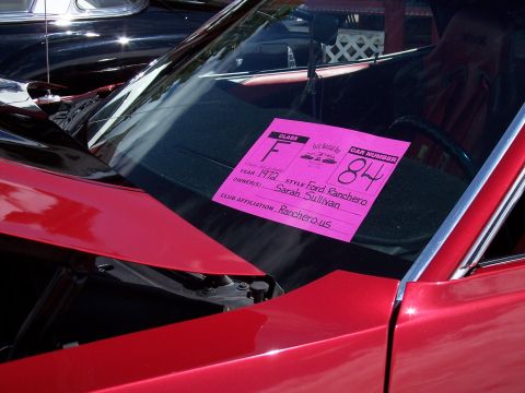1972 Ford Ranchero - A pink card on the windshield of a red car details its year, style, owner, and car number.