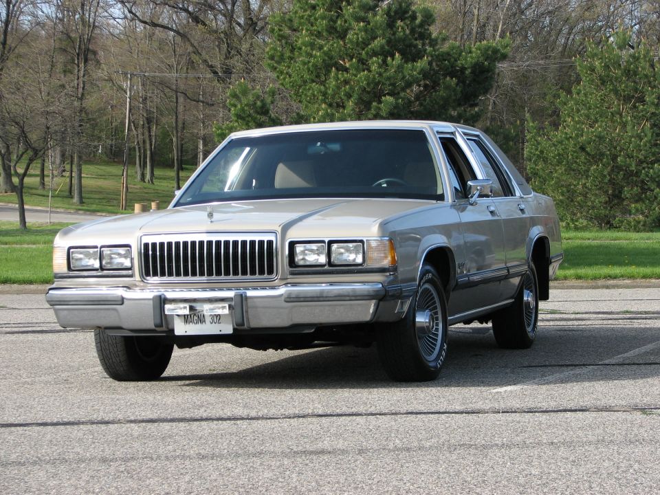 Silver 1980s Mercury Grand Marquis sedan parked on asphalt, front 3/4 view