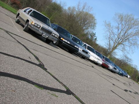 2003 Ford Crown Victoria - A line of sedans, including a silver one with a prominent chrome grille, are parked in an outdoor lot.