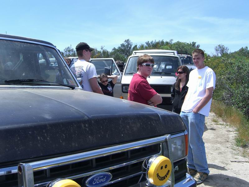1980 Ford F-250 front end with smiley face lights, people standing around other vehicles