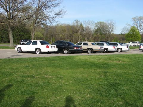 2003 Ford Crown Victoria - A white 2003 Ford Crown Victoria sedan is parked in a lot with several other vehicles.