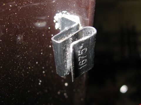 1974 Ford F-100 - A metal clip with the number 1675 stamped on its side is attached to a dark, speckled surface.