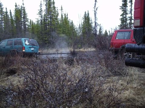 1986 Ford F-150 - Two SUVs appear stuck in a wooded, off-road environment.