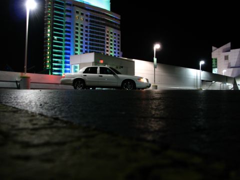 2003 Ford Crown Victoria - A white 2003 Ford Crown Victoria is parked in front of a brightly lit building at night.