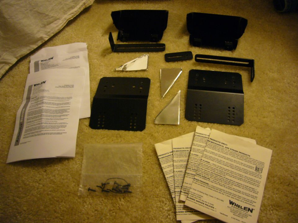 Whelen siren mounting brackets, screws, and instruction manuals laid out on a carpeted surface