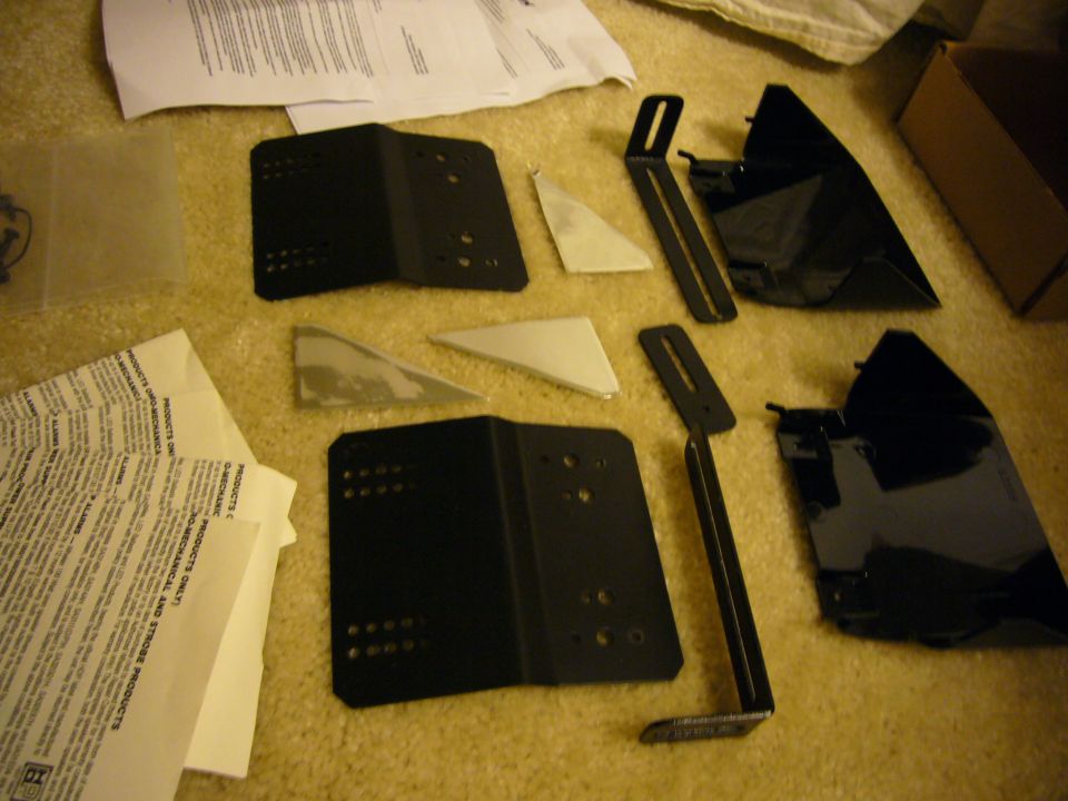 Various black metal brackets, triangular metal pieces, and instruction papers are laid out on a carpeted surface