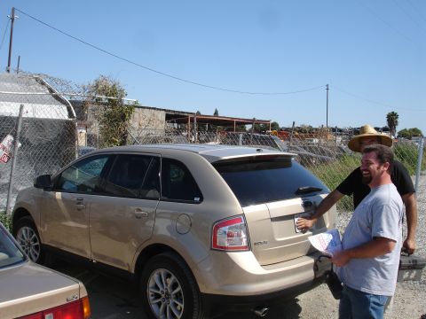 1993 Ford Taurus - Two men are standing behind a tan SUV in what appears to be a junkyard or auto repair lot.