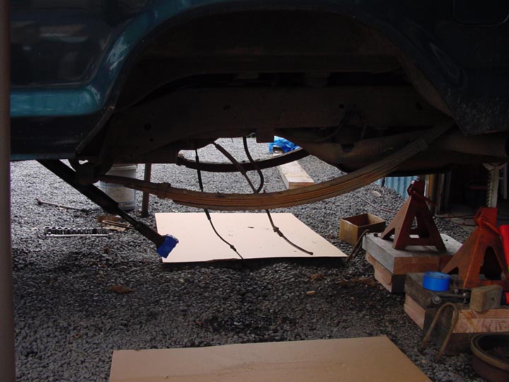 Underside of vehicle showing rear axle, leaf springs, and suspension components. Vehicle is raised on jack stands