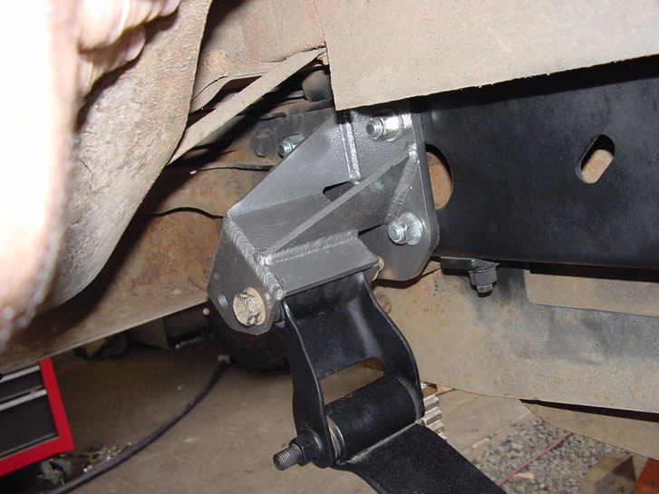 Close-up of a custom-welded metal bracket attached to a vehicle's frame, near suspension components