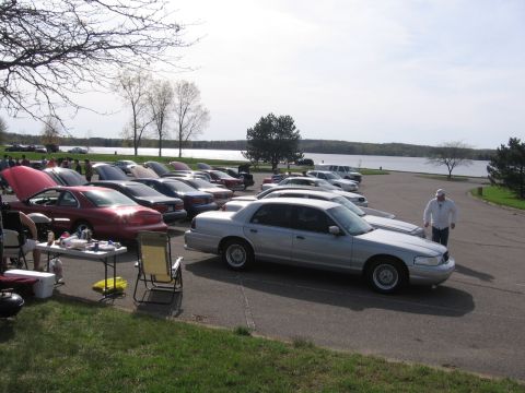 1988 Mercury Grand Marquis - Several cars are parked in a lot near a body of water, with a man walking near a silver sedan.