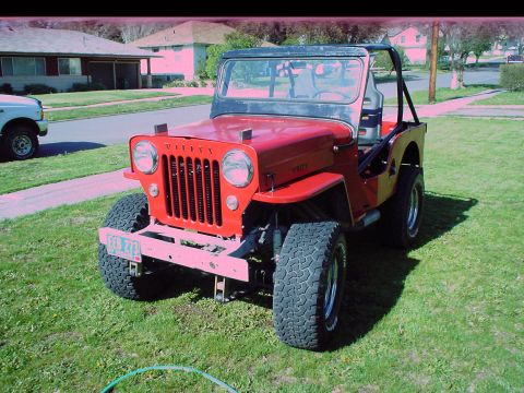 1954 Jeep CJ5 - A red Jeep CJ is parked on a grassy lawn in front of houses.