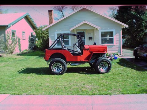 1954 Jeep CJ5 - A red Jeep with a roll cage sits on a lawn in front of a residential house.