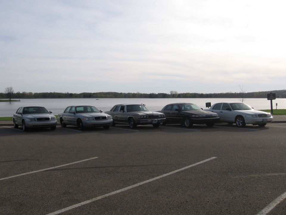 five sedans parked in a row, lake in background