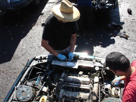 1993 Ford Taurus - Two men are working on the engine of a car in a junkyard.