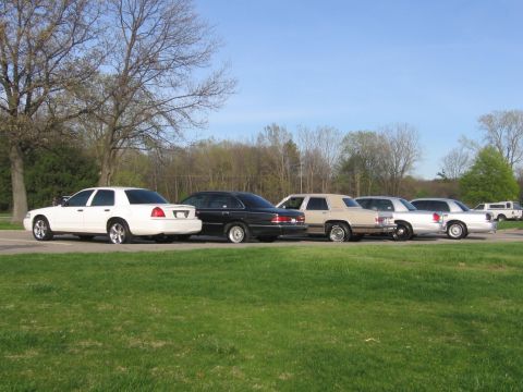 1988 Mercury Grand Marquis - Several sedans, including a white 1988 Mercury Grand Marquis, are parked in a line on a grassy area.