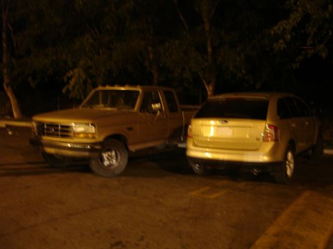 1993 Ford Taurus - A gold SUV and a pickup truck are parked side-by-side at night.