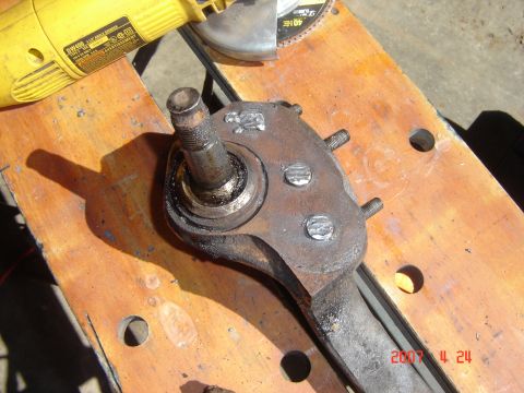 1993 Ford Bronco - A suspension knuckle sits on a wooden workbench next to a grinder and cutting disc.
