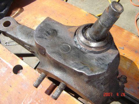 1993 Ford Bronco - Rusty steering knuckle assembly, likely from a truck or SUV, resting on a wooden surface.