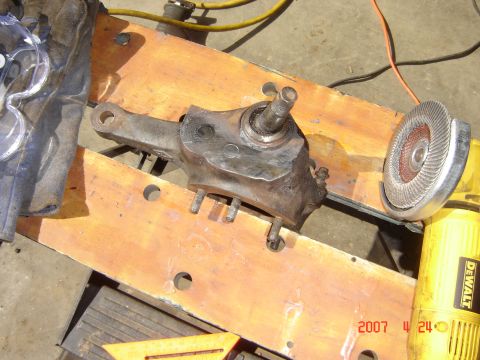 1993 Ford Bronco - A metal vehicle steering knuckle sits on a wooden surface next to a grinding tool.