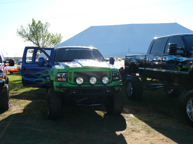 Green and blue Ford F-Series truck with flames, open driver's door, three spotlights on grille