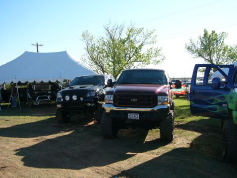 1978 Ford Bronco - A lifted maroon Ford F-250 Super Duty is parked at an outdoor event, with other modified trucks visible.