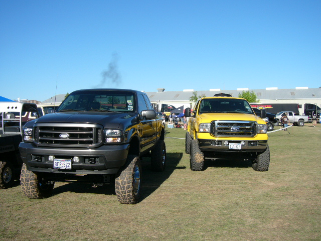 Two lifted Ford trucks, one gray and one yellow, parked on grass
