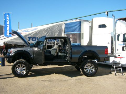 1978 Ford Bronco - Lifted pickup truck with open doors and hood, parked beside a semi-trailer with Toyo Tires branding.