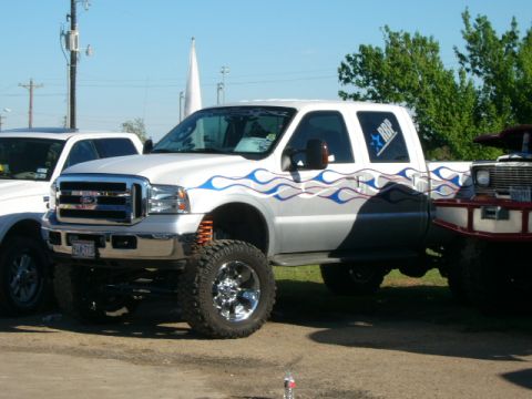 1978 Ford Bronco - White Ford F-250 Super Duty pickup truck with custom flame decals and lifted suspension is parked at an outdoor event.