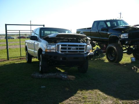1978 Ford Bronco - Two Ford F-Series trucks, one silver and one black lifted, are parked on grass.