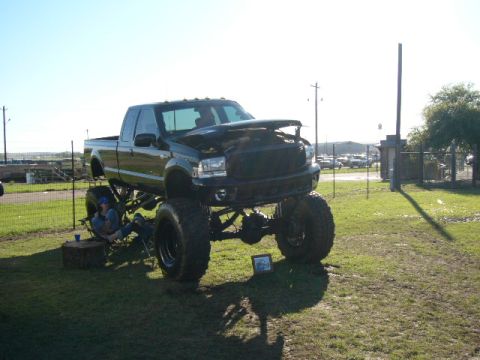 1978 Ford Bronco - A heavily modified black pickup truck is parked on a grassy field under a clear sky.