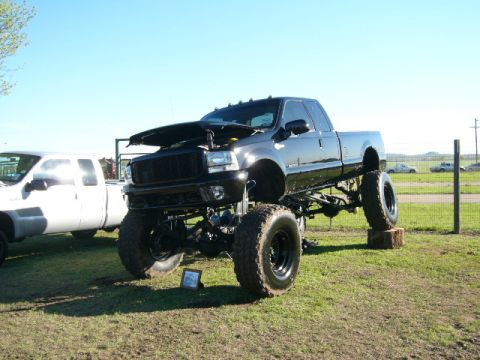 1978 Ford Bronco - A heavily modified black pickup truck is displayed with its hood up, alongside another truck on a sunny day.