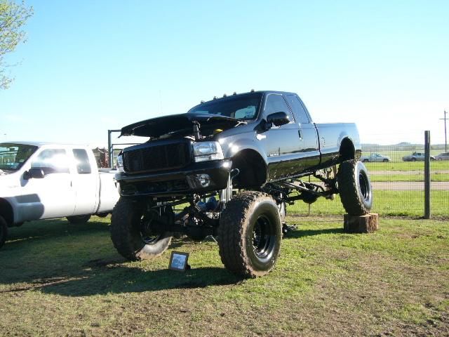 Black extremely lifted Ford Super Duty extended cab with hood open on show grass