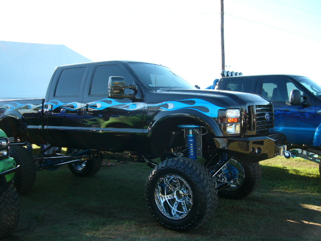 Lifted black Ford F-Series truck with blue flames and chrome wheels, parked next to a blue truck