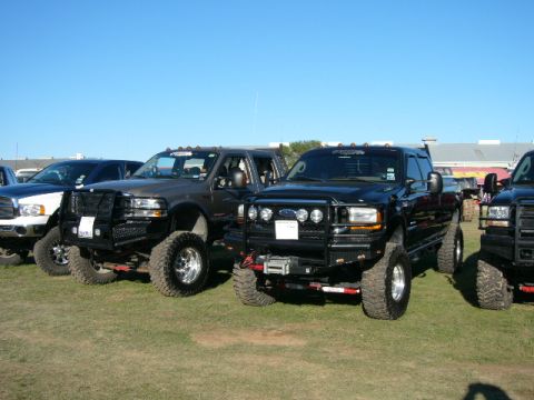 1978 Ford Bronco - Multiple lifted Ford trucks are parked on a grassy field on a sunny day.