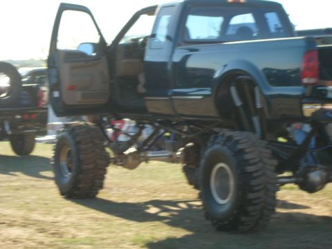 1978 Ford Bronco - Modified pickup truck with extreme lift and oversized tires, parked outdoors with another vehicle nearby.