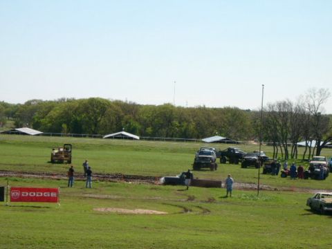 1978 Ford Bronco - A muddy field hosts a gathering of off-road vehicles and spectators, with a prominent Dodge banner in the foreground.